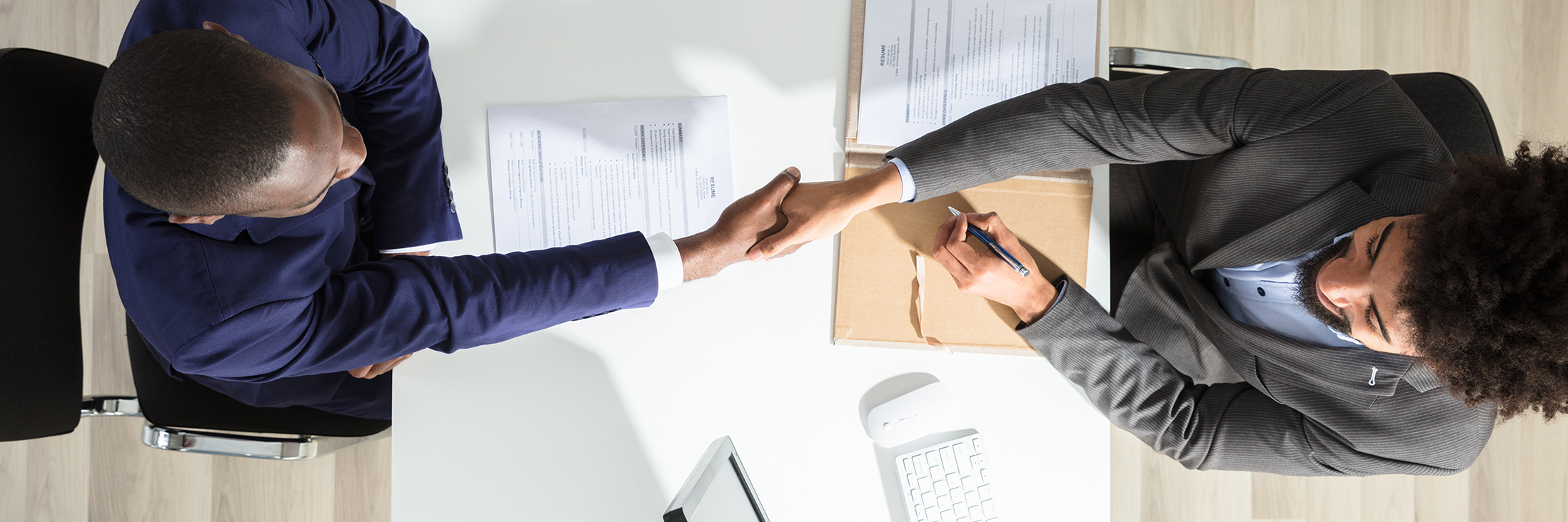 Young Businessman Shaking Hand With Candidate Over White Desk