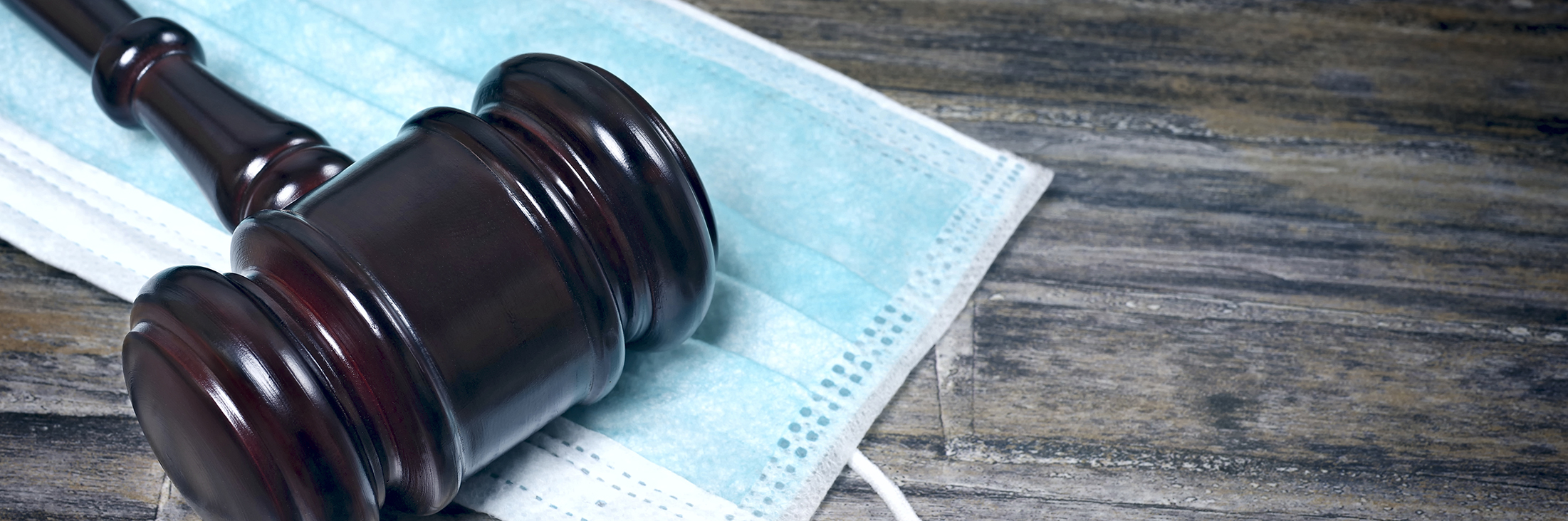 Gavel Resting On A Protective Mask on a wooden table.